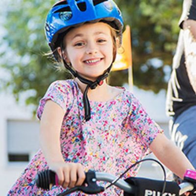 Ein lächelndes Kind mit blauem Fahrrad-Helm umgreift einen Fahrradlenker
