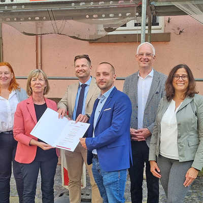Vor dem vor rund 100 Jahren errichteten Gebäude Magnerichstraße 9-11 überreicht Finanzministerin Doris Ahnen( 2. v. l.) den Förderbescheid an Steve Klein und Stefan Blankenberg von der WIT (3. und 4. v. l.) . Mit dabei sind außerdem ISB-Vorstandsmitglied Sandra Baumbach, OB Wolfram Leibe und gbt-Vorstandsmitglied Sybille Jeschonek (v. r.).