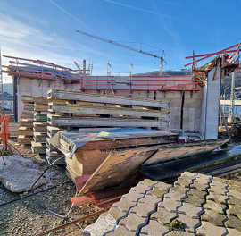 Verschiedene Baustoffe lagern auf einer Baustelle, im Hintergrund steht ein Kran.