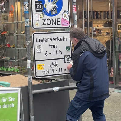 Norbert Braun vom Bürgerservice kämpft mit der mühsamen Entfernung verschiedener Aufkleber von einem Verkehrsschild.